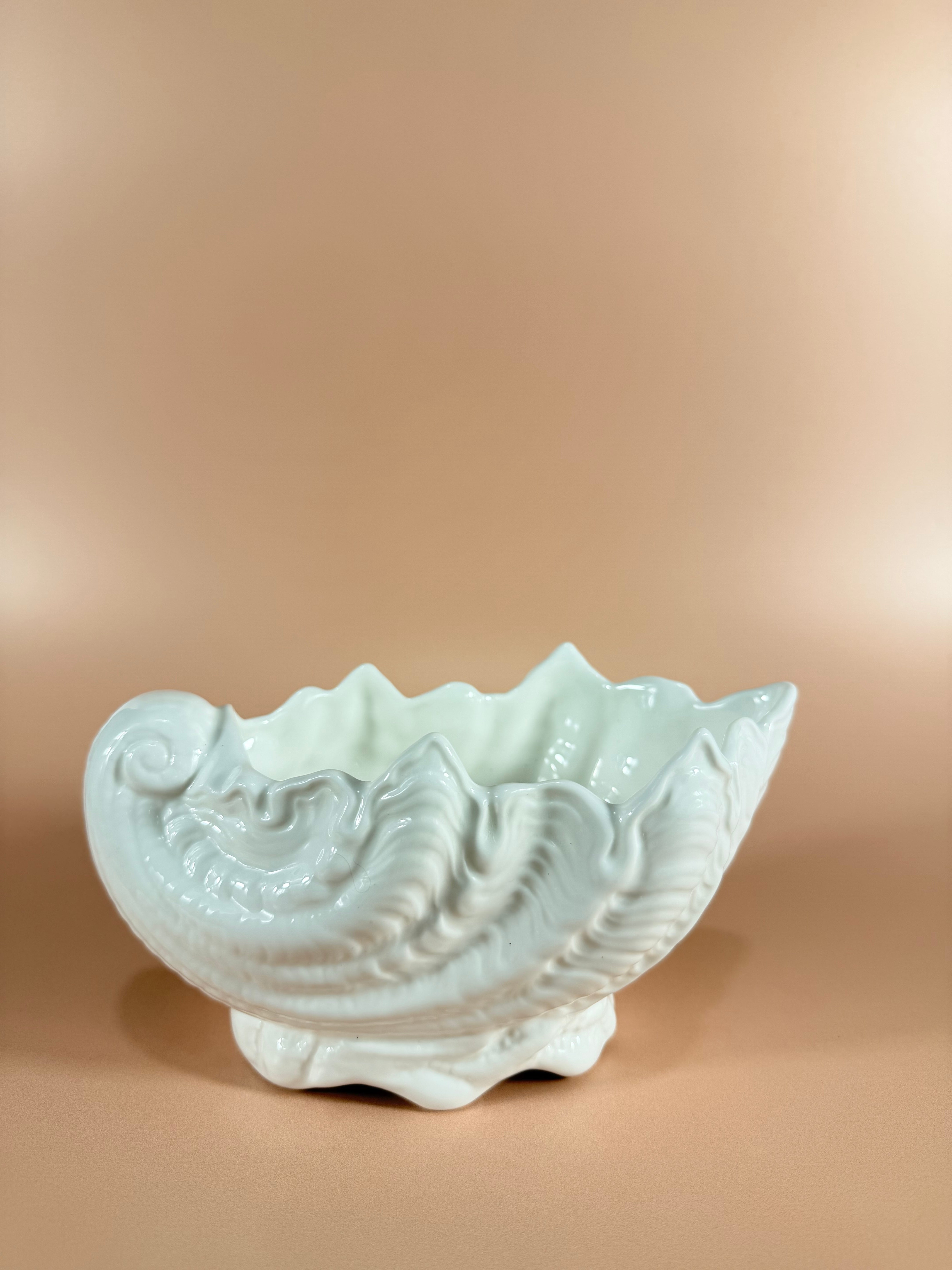 A white ceramic decorative bowl with a sculpted, textured surface resembling layered leaves or petals, set against a warm beige gradient background.