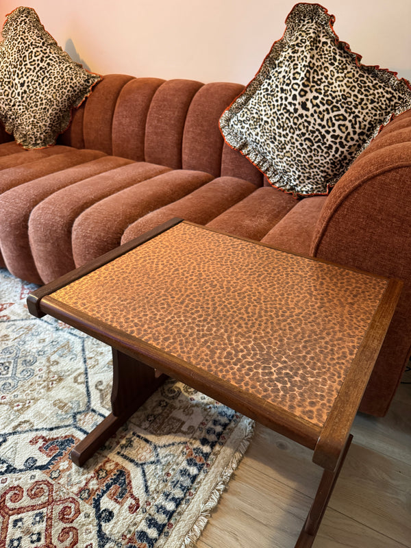 Brown sofa with leopard print pillows and a matching side table in a living room setting.