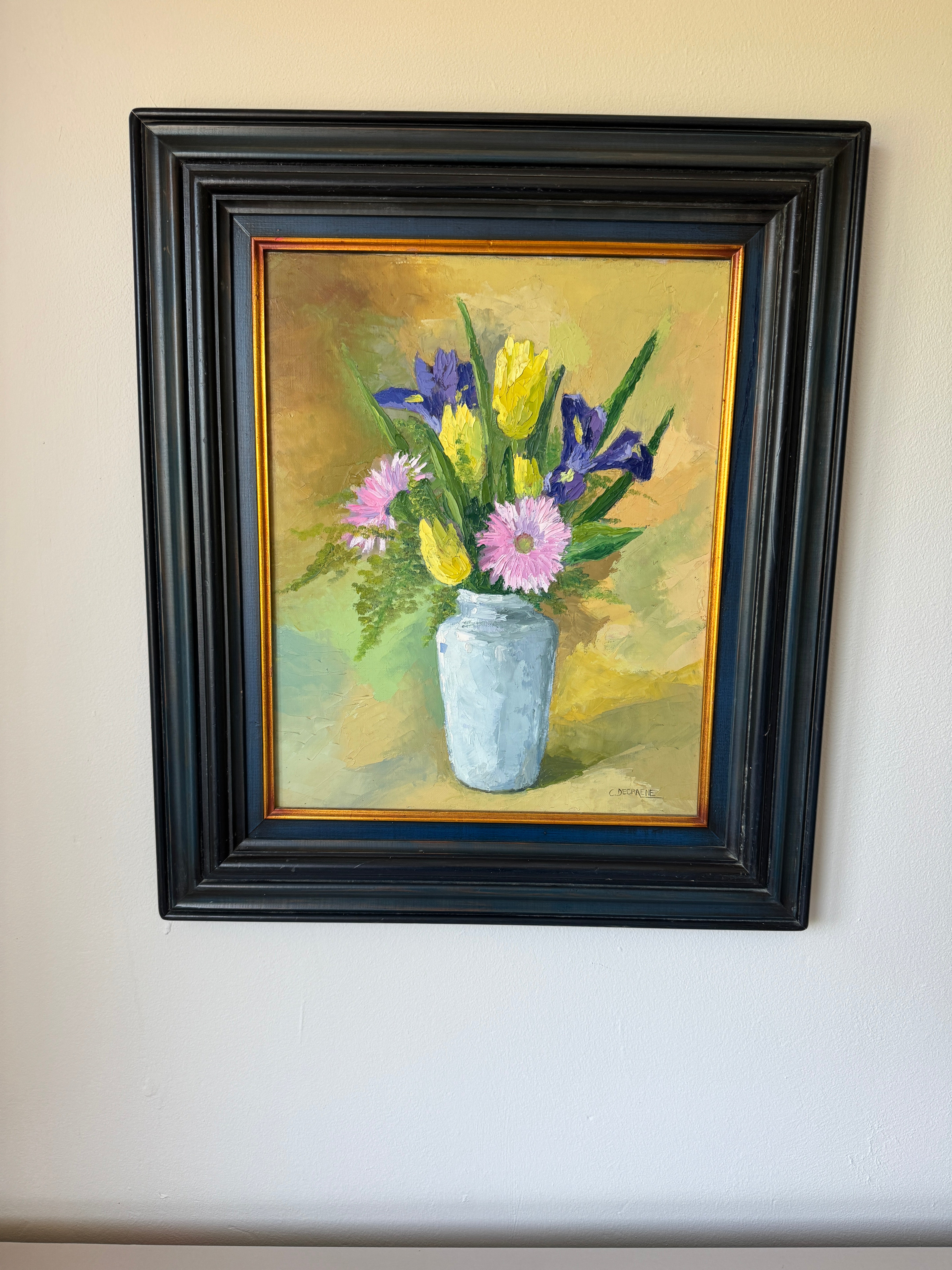 Framed painting of a bouquet of flowers in a vase on a beige wall.