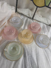 Set of pastel-colored teacups and saucers on a textured surface with a stained glass window in the background.
