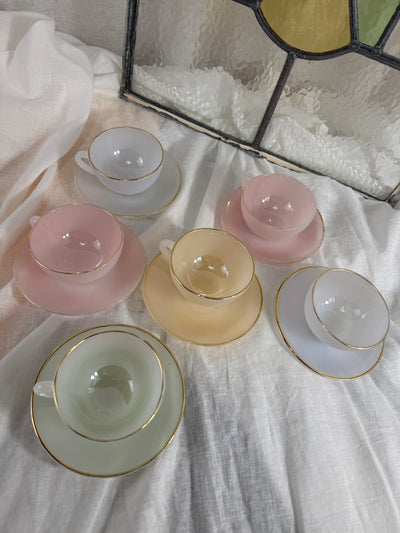 Set of pastel-colored teacups and saucers on a textured surface with a stained glass window in the background.