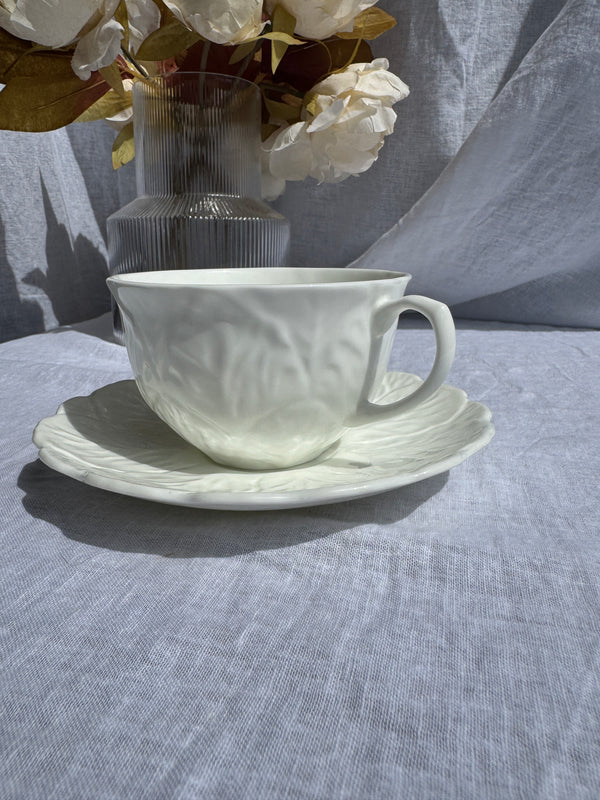 White ceramic teacup and saucer on a textured gray surface with flowers in the background.